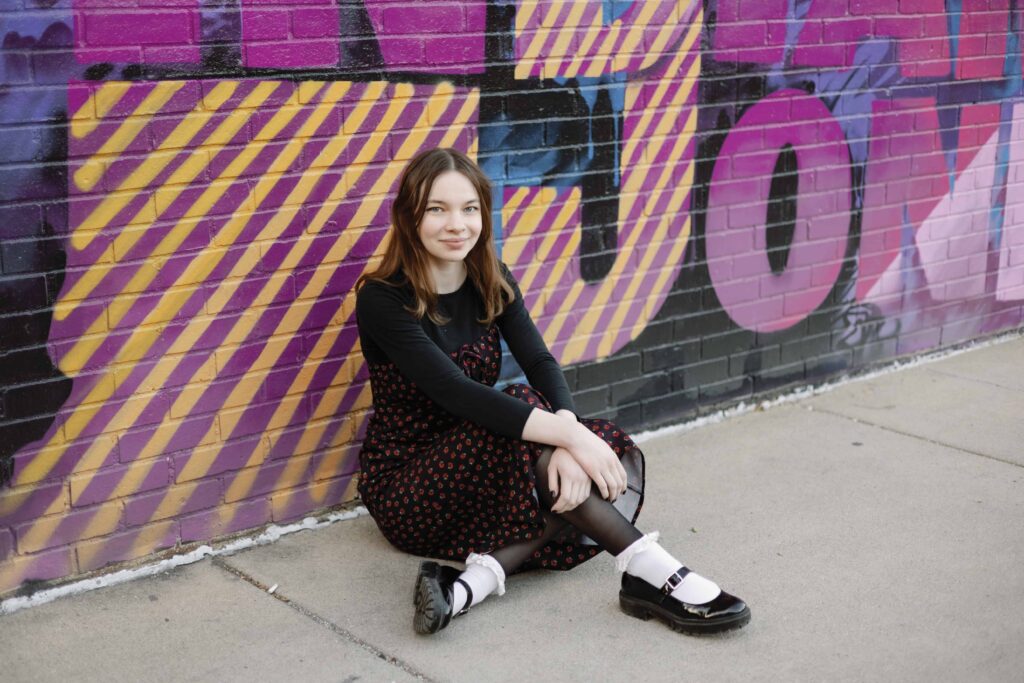 Artsy senior picture of high school senior girl sitting against graffiti wall in Broad Ripple